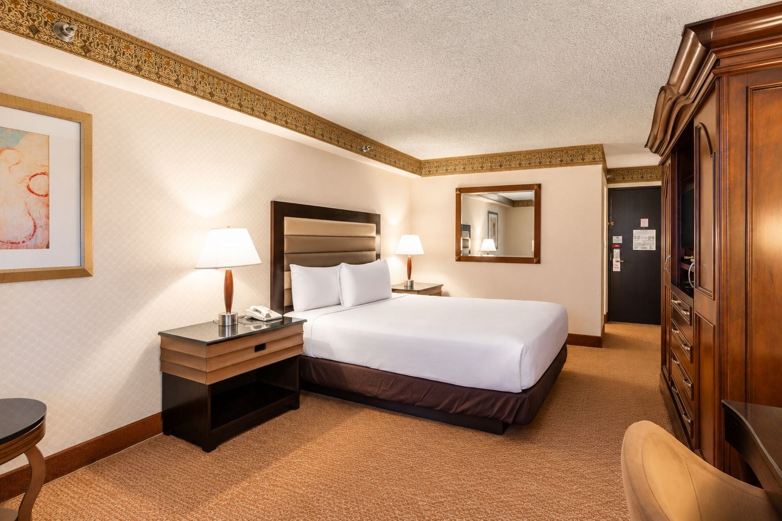 A hotel room with a bed, bedside tables, lamps, a mirror, and a wardrobe.