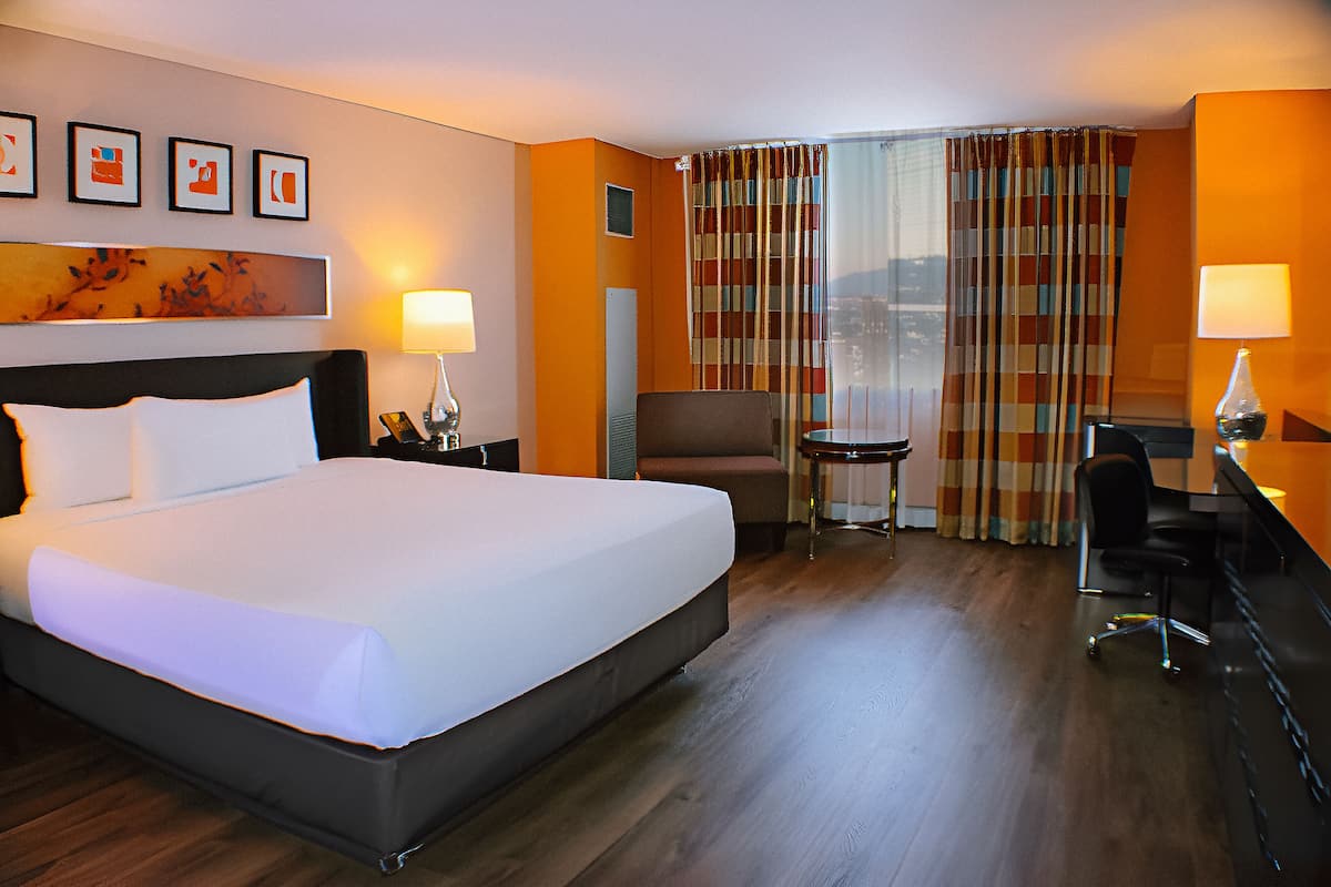 Ein Hotelzimmer mit einem großen Bett, einem Schreibtisch, einem Stuhl und einem kleinen Tisch.