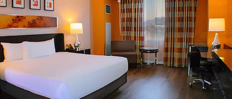 A hotel room with a large bed, a desk, a chair, and a small table.