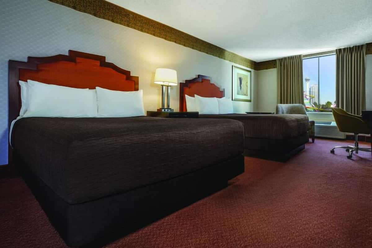 Ein Hotelzimmer mit zwei Betten, einem Schreibtisch, einem Stuhl und einem großen Fenster mit Blick auf einen Turm.