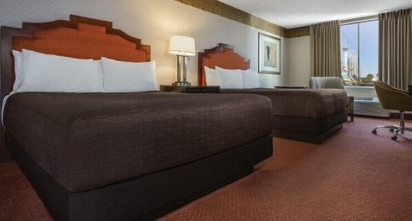 A hotel room with two beds, a desk, a chair, and a large window with a view.