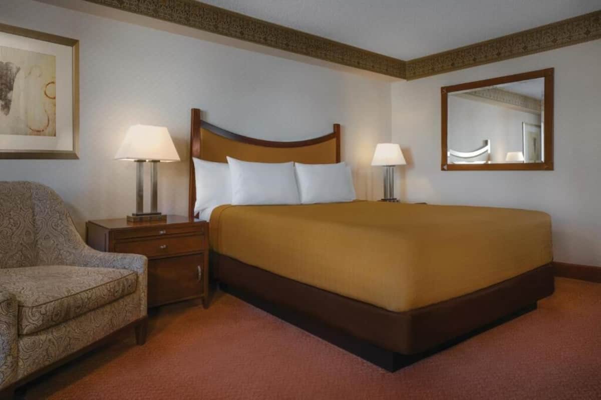 Ein Hotelzimmer mit einem großen Bett, zwei Nachttischen mit Lampen, einem Sessel und einem Spiegel an der Wand.