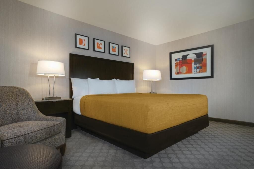A hotel room with a bed, two bedside lamps, a chair, and framed artwork on the walls.