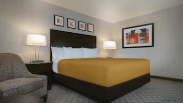 A hotel room with a bed, two bedside lamps, a chair, and framed artwork on the walls.
