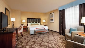 A hotel room with a bed, a desk with a chair, a television, and a sofa.