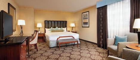Una habitación de hotel con cama, un escritorio con silla, televisión y sofá.