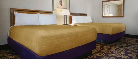 A hotel room with two beds, a large mirror, a framed artwork on the wall, and a patterned carpet.
