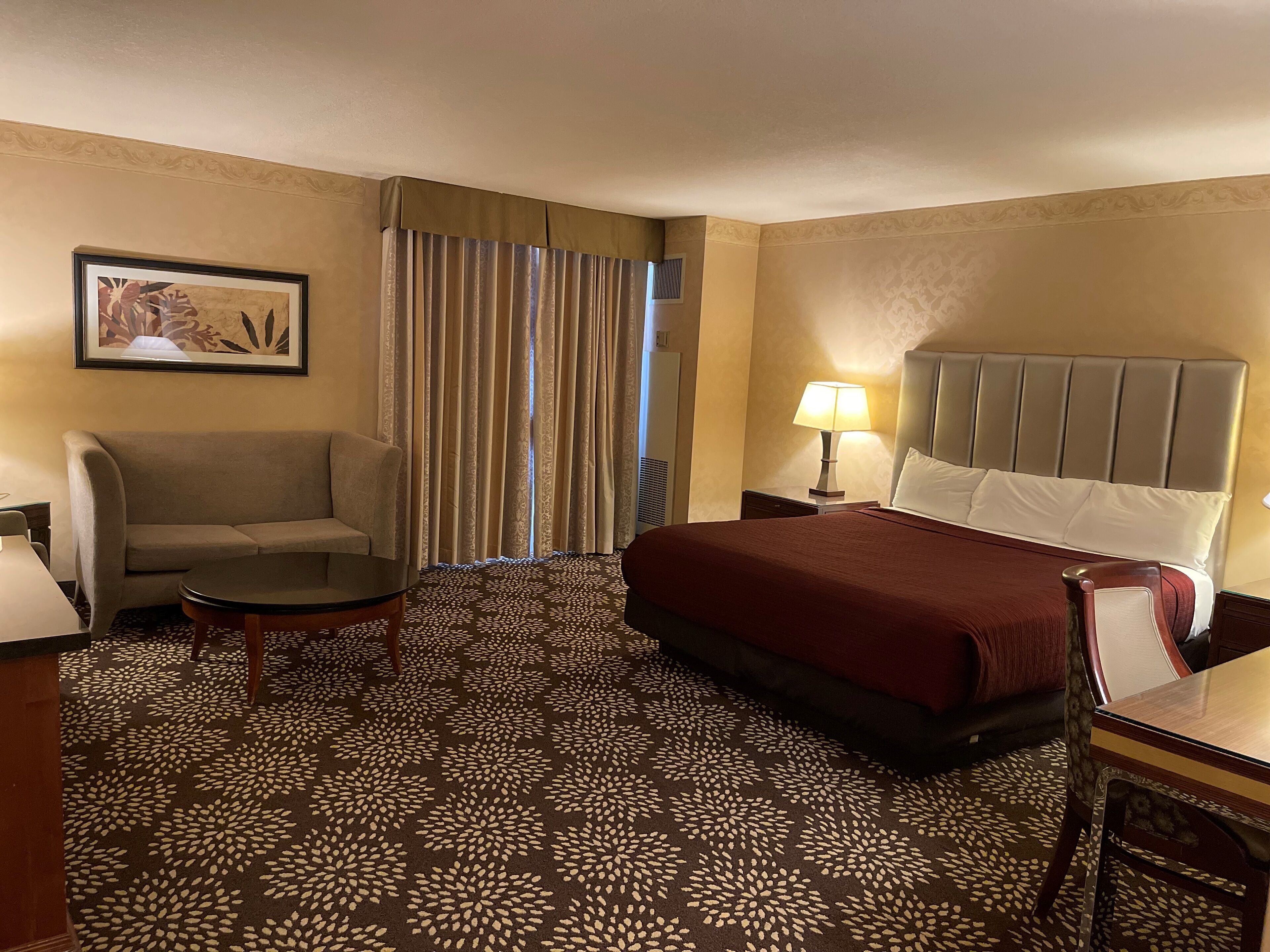 A hotel room with a bed, a sofa, a small table, a lamp, and a framed picture on the wall.