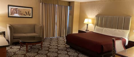 Habitación de hotel con una cama, un sofá, una mesita, una lámpara y un cuadro en la pared.