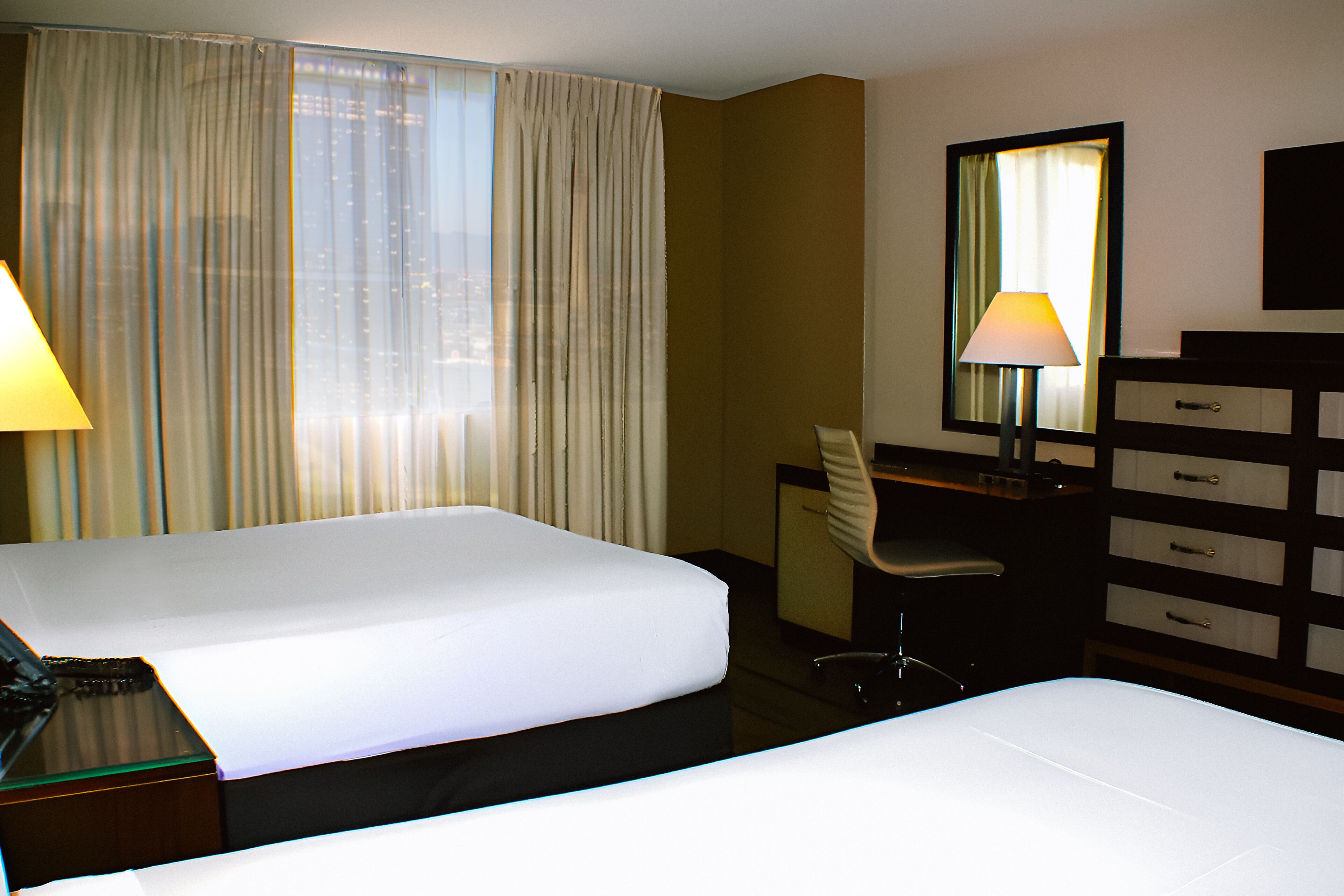 Ein Hotelzimmer mit zwei Betten, einem Schreibtisch, einem Sessel, einer Kommode und einem Fenster mit Vorhängen.