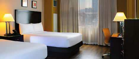 A hotel room with two beds, a desk, a chair, and a large window with curtains.