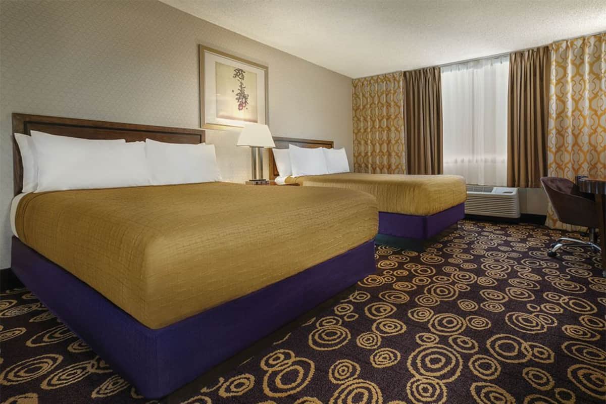 Ein Hotelzimmer mit zwei Betten, einem Schreibtisch, einem Sessel und einem gemusterten Teppich.
