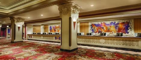A spacious lobby with ornate columns, a patterned carpet, and a reception desk with a colorful mural.