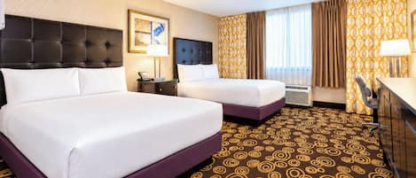 Quarto de hotel com duas camas, uma mesa, uma cadeira e um tapete estampado.