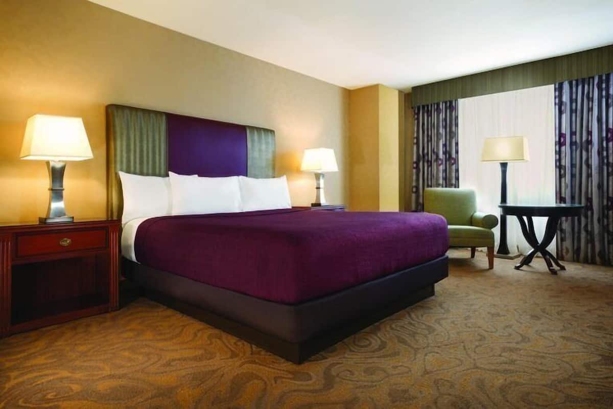 Ein Hotelzimmer mit einem großen Bett, zwei Nachttischen mit Lampen, einem grünen Sessel und einem kleinen Tisch ebenfalls mit einer Lampe.