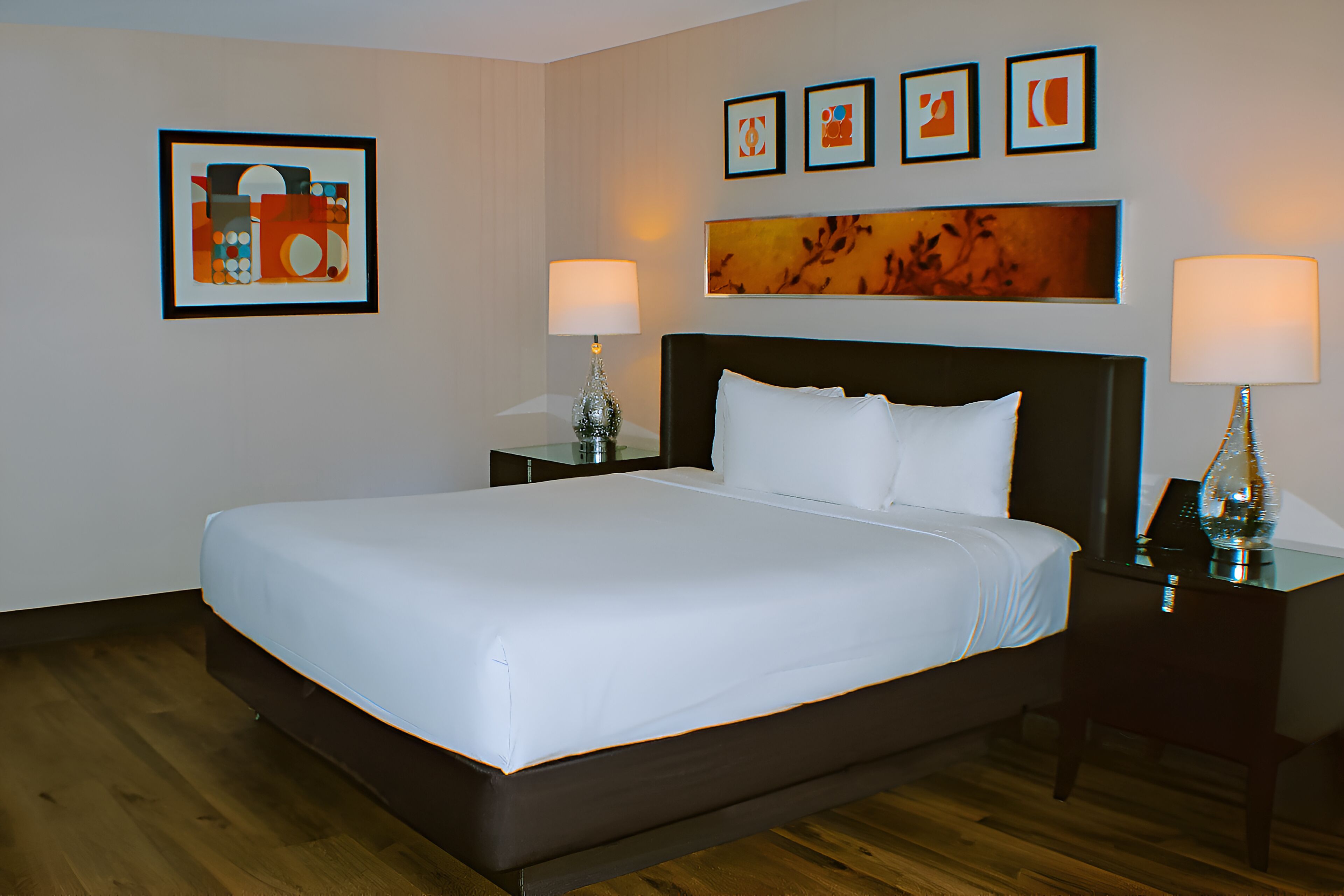 A hotel room with a large bed, two bedside tables with lamps, and artwork on the walls.