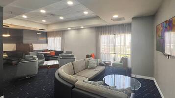 A modern hotel lobby with a curved sofa, armchairs, a coffee table, and a large window with curtains.