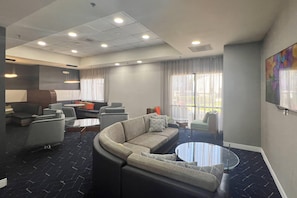 Un moderno vestíbulo de hotel con un sofá curvo, sillones, una mesa de centro y un gran ventanal con cortinas.
