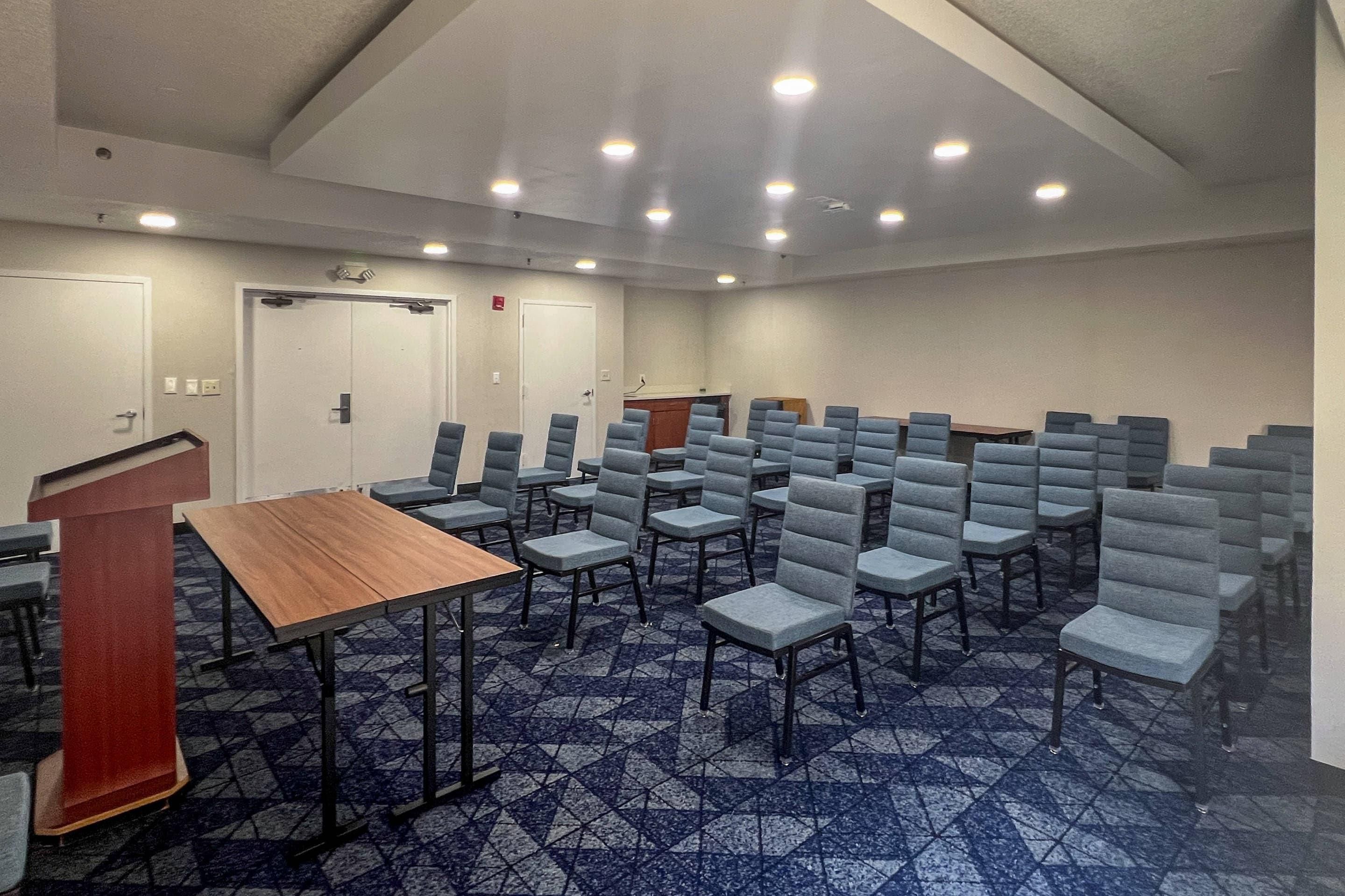 Een vergaderzaal met rijen stoelen, een spreekgestoelte en een vloerbedekking.