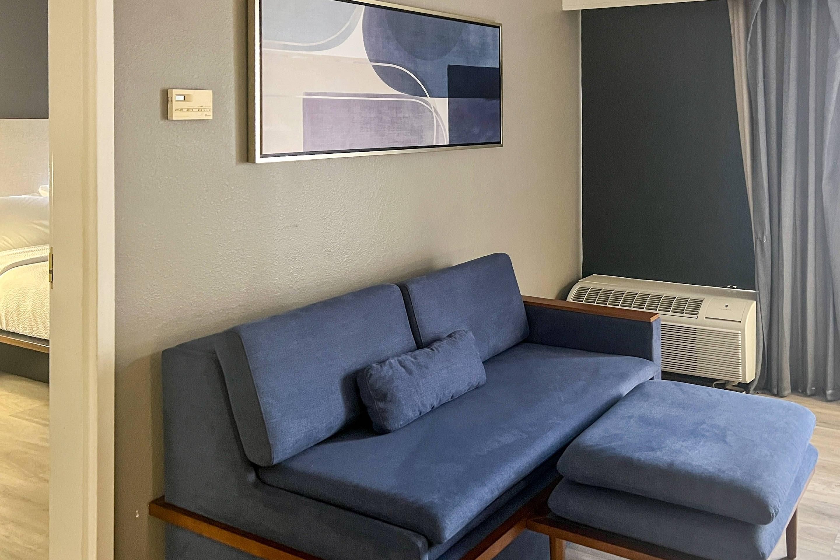 A modern room with a grey sofa, a wall-mounted air conditioner, and a partial view of a bed.