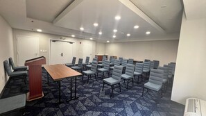 Une salle de conférence avec une longue table, de nombreuses chaises, un pupitre et une porte.