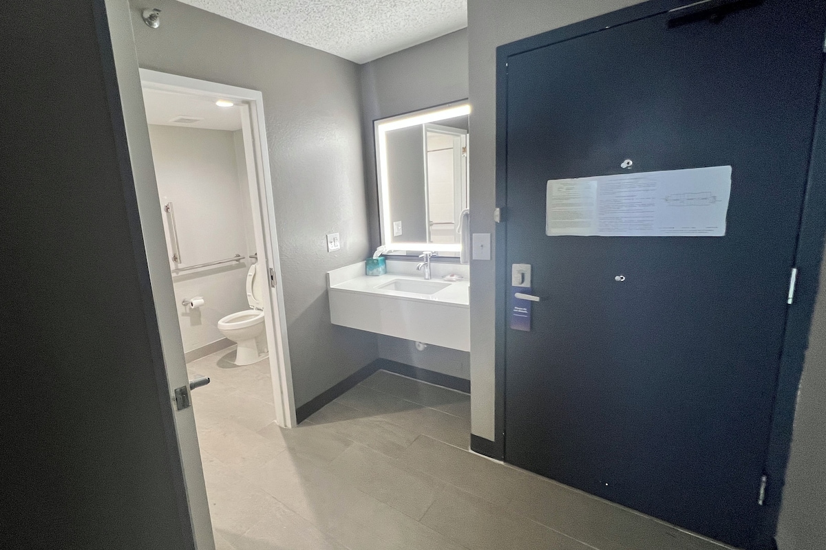 Een badkamer met toilet, wastafel en spiegel. Deur met een bordje erop.