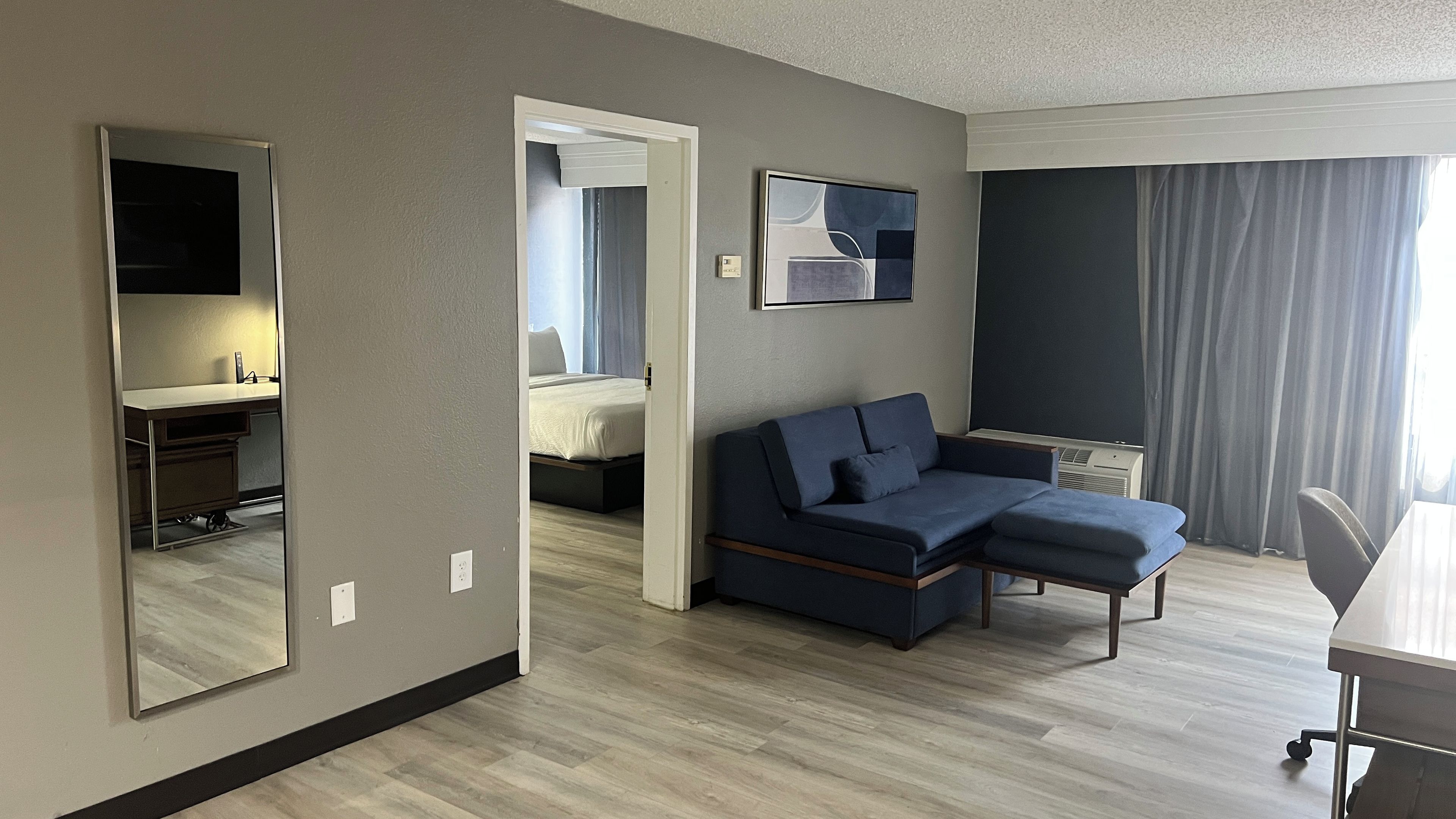 Una habitación de hotel moderna con una cama grande, un sofá, un escritorio y un espejo amplio.