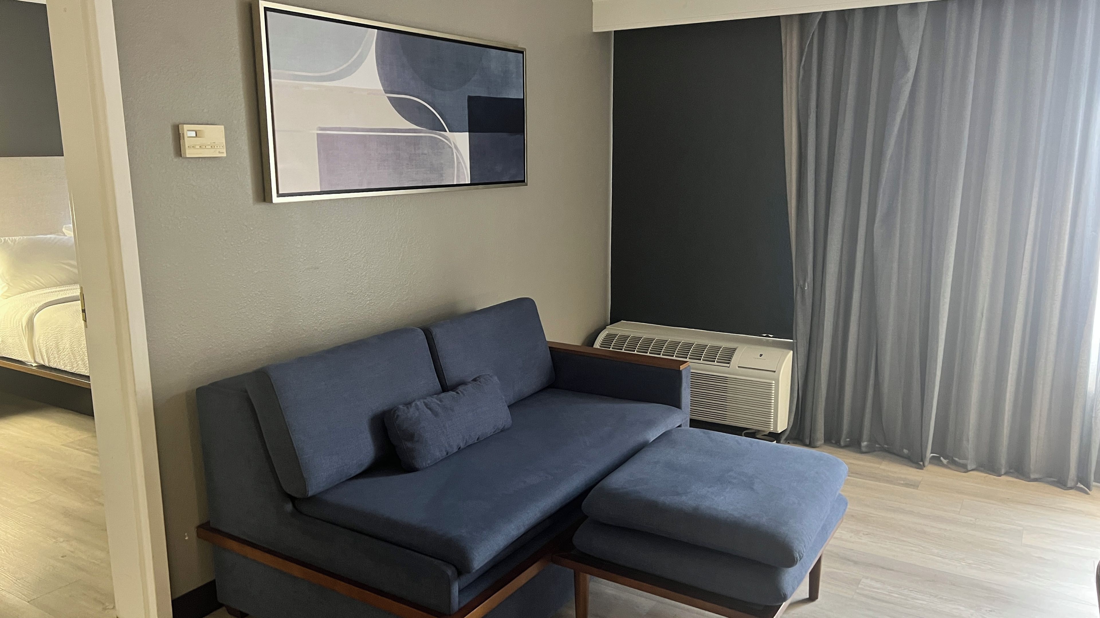 Un soggiorno moderno con un divano componibile, un condizionatore d'aria a muro e un grande quadro astratto.