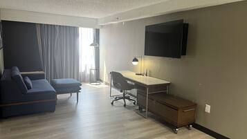 Ein modernes Hotelzimmer mit Sofa, Schreibtisch, Stuhl und einem wandmontierten Flachbildfernseher.