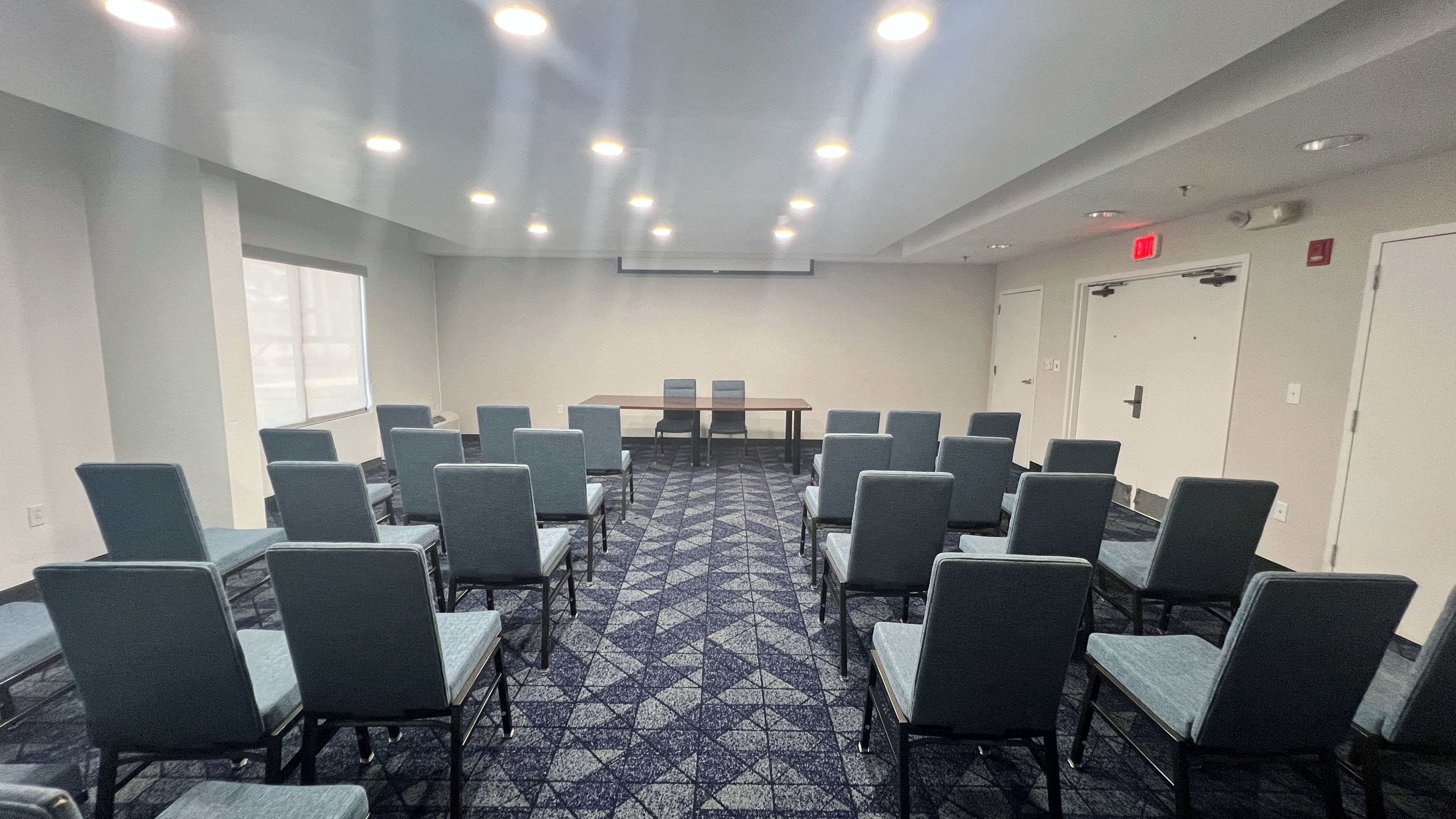 Un salón de conferencias con una larga mesa y sillas, piso alfombrado e iluminación en el techo.