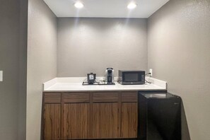 Una pequeña kitchenette con microondas, cafetera y tostadora en la encimera.