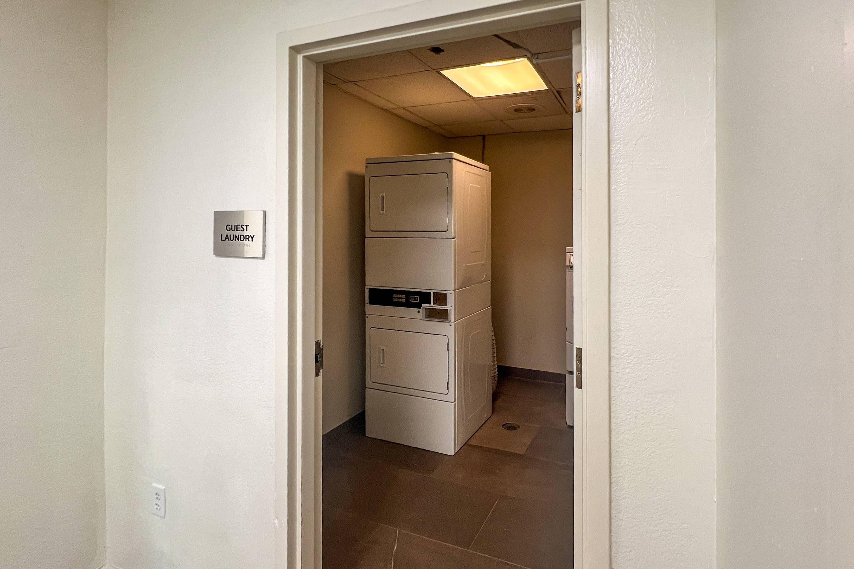 A laundry room with a sign indicating it's for guests, a stacked washer and dryer, and a door with a handle.