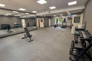 Un gimnasio con equipamiento de ejercicio, un espejo y una cinta de correr.