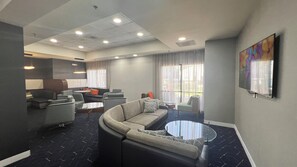 Een moderne hotel lobby met een gebogen bank, een ronde salontafel en een eetgedeelte met een gezellige zithoek.