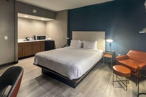 Una habitación de hotel con cama, escritorio, silla y kitchenette.