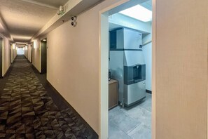 Ein Hotelkorridor mit Steinfliesen, einem Kühlschrank und einer Tür zu einem Zimmer.