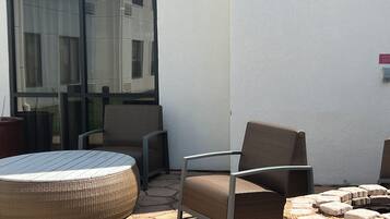 Uma área externa com mobiliário de vime e uma mesa de vidro, localizada ao lado de um edifício com grandes janelas.