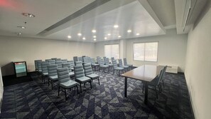 Une salle de conférence avec des rangées de chaises, une table et de grandes fenêtres.