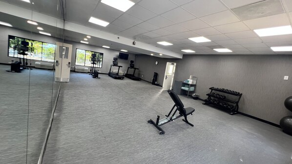 Une salle de sport équipée de matériel d’exercice, dotée d’un mur recouvert de miroirs et d’un sol recouvert d’un tapis gris.