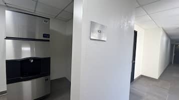 Ein Flur mit einem Edelstahlkühlschrank, einem Schild, das einen Eisautomaten anzeigt, und einer Tür zu einem anderen Raum.