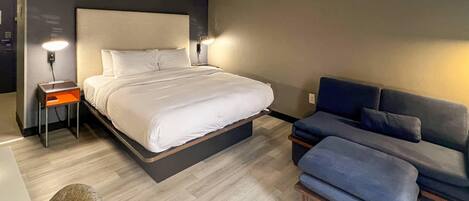 A modern hotel room with a bed, bedside tables, a sofa, and a chair.