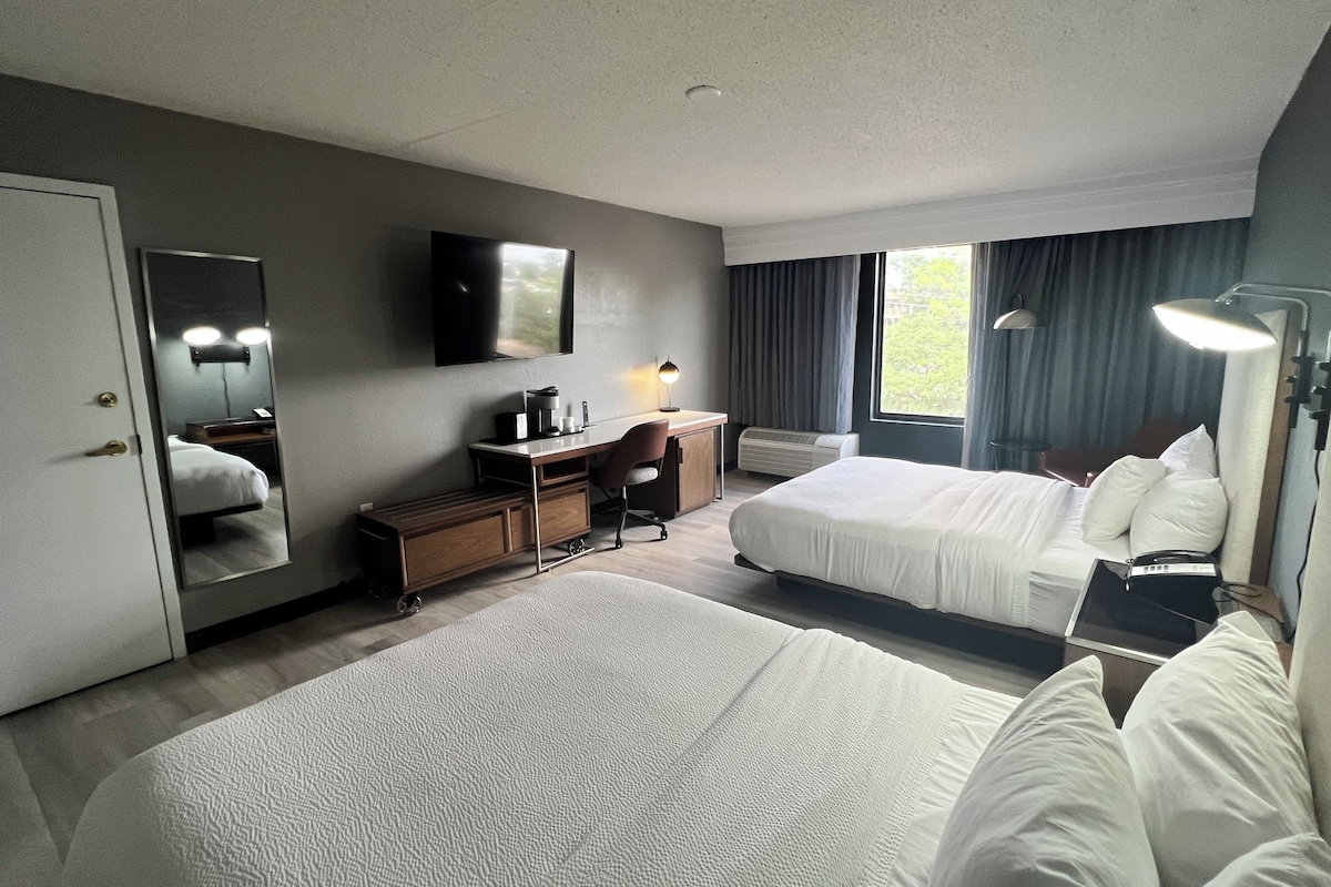 Een hotelkamer met twee bedden, een bureau, een stoel, een televisie en een raam met gordijnen.