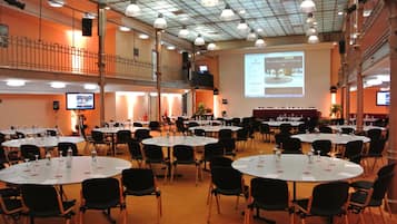 Un salón de conferencias con varias mesas redondas, sillas negras y una pantalla grande mostrando una presentación.