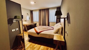 Habitación de hotel con cama, escritorio, silla y ventana con cortinas.