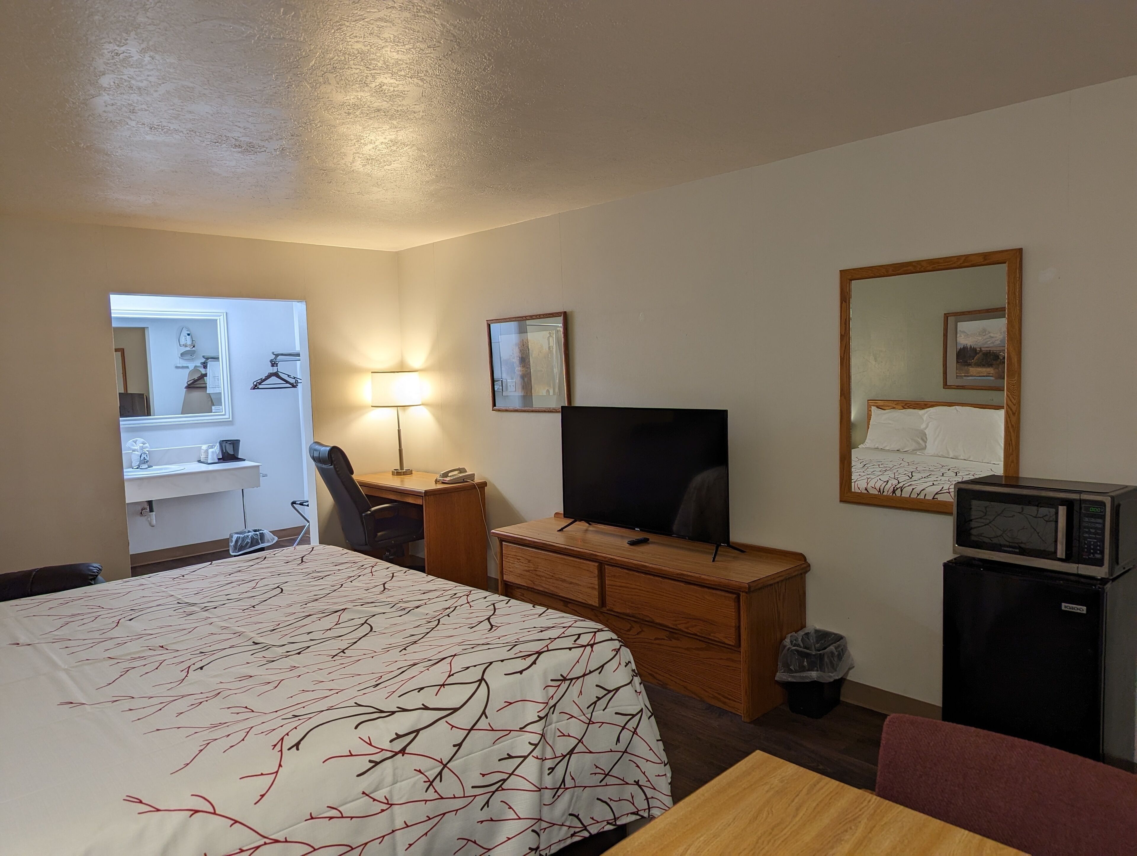 Ett hotellrum med en säng, ett skrivbord med en dator, en tv, en mikrovågsugn och en liten papperskorg.