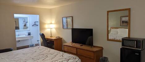 Ein Hotelzimmer mit Bett, Schreibtisch mit Computer, Fernseher, Mikrowelle und kleinem Mülleimer.
