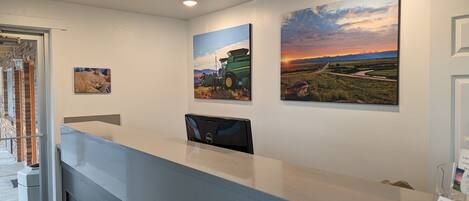 A reception desk with a computer, three landscape paintings, and a door to the left.