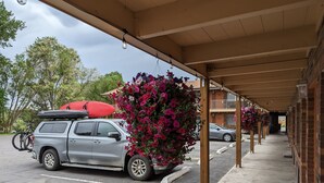 A covered parking area with a car and a kayak on the roof, surrounded by blooming flowers. - Henry's Fork Inn (St. Anthony)