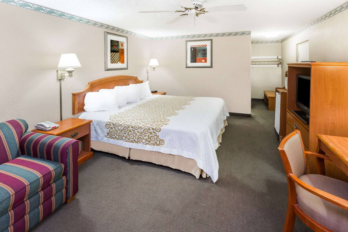A hotel room with a bed, a TV, a desk, a chair, and a lamp.
