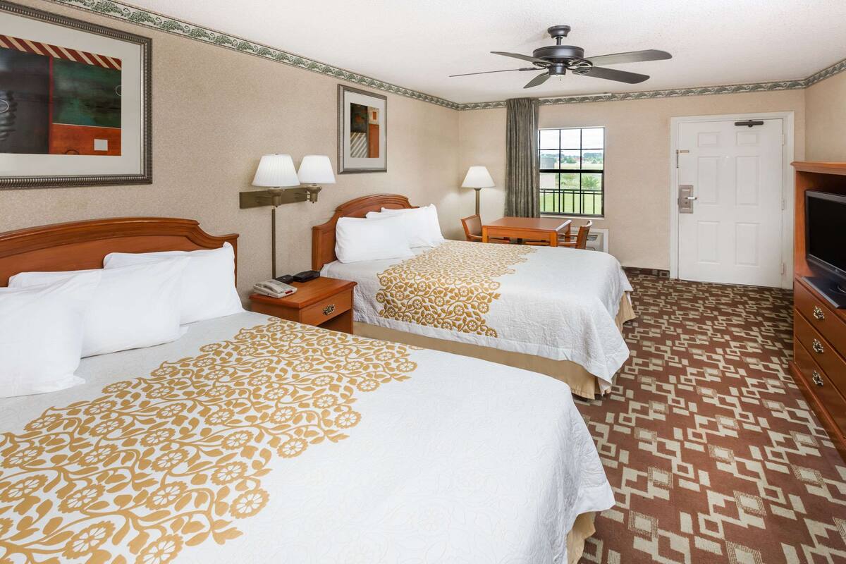 A hotel room with two beds, a desk, a television, and a ceiling fan.